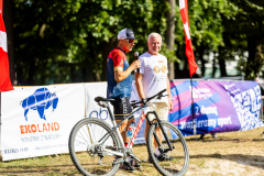 Andrzej Rolla w obecności konferansjera który trzyma przed sobą rower, obaj stoją na dworze  w letni dzień