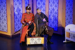 Dwóch mężczyzn przebranych za sarmatów siedzi na scenie teatralnej, dookoła nich scenografia stylizowana na wnętrze szlacheckiego budynku