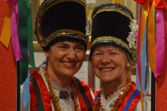 Zdjęcie portretowe dwóch kobiet w strojach ludowych, obie mają na głowach charakterystyczne wysokie czapki z przyczepionymi kolorowymi wstążkami