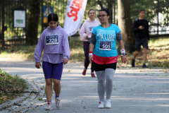 Dwie panie w stroju sportowym, przechodzą przez park, na koszulkach mają naklejki z numerami zawodnika