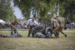 Rekonstrukcja bitwy z czasu drugiej wojny światowej, kilku mężczyzn z bronią  zbiera się dookoła motocyklu