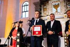 Członek Zarządu Województwa Lubelskiego Marcin Szewczak stoi we wnętrzu synagogi i prezentuje ramkę z umieszczony wewnątrz medalem 550 -lecia