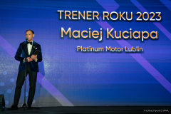 Mężczyzna trzymając statuetkę przemawia do mikrofony, za nim na dużym ekranie wyświetla się napis trener roku 2023 Maciej Kuciapa Platinum Motor Lublin