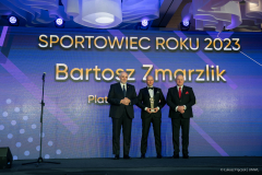 Marszałek Województwa Lubelskiego w towarzystwie dwóch mężczyzn , za nimi na ekranie wyswietla się napis sportowiec roku 2023 Bartosz Zmarzlik