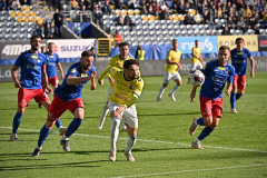 Trwający mecz piłkarski, Zawodnicy przeciwnych drużyn sa rozstawienie na róznych pozycjach na boisku, dwóch z nich biegnie do przodu żeby przejąć piłkę