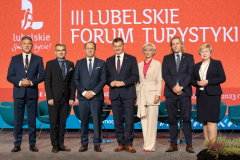 Dwie kobiety i pięciu mężczyzn pozuje do zdjęcie stojąc na scenie, za nimi na ekranie wyswietla się napis III Lubelskie Forum Turystyki