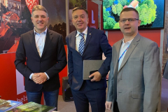 Trzech mężczyzn pozuje wspólnie do zdjęcia za nimi widać ekran wyświetlający film z krajobrazami województwa lubelskiego