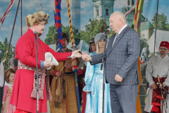 Mężczyzna ubrany w strój sarmacki stoi na scenie i przekazuje symboliczny klucz wójtowi Jerzemu Trociowi