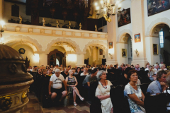 Wewnątrz kościoła w ławkach siedzi kilkadziesiat osób, słuchaczy koncertu