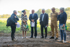 Przedstawiciele władz samorzadowych oraz OSP w trakcie rozmowy. Sześć osób stoi w okolicy terenów leśnych w letni dzień