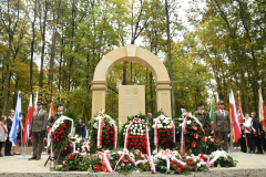 Widok na pomnika pamięci pomordowanych Żydów  oraz czterech żołnierzy pełniących przy nim wartę i około dziesięciu złożonych wieńców pod pomnikiem