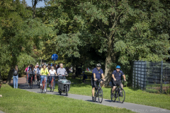 Przejazd rowerowy prowadzony przez Macieja Lubasia przejeżdża ścieżką rowerową otoczoną terenami zielonymi.