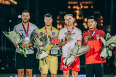 Czterech sportowców stoi wspólnie na podium, wszyscy trzymają w rękach kwiaty i prezentują zdobyte medale