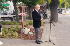 Mężczyzna stojący obok nowo odsłoniętej tablicy przemawia do zgromadzonych korzystając ze stojącego mikforonu.
