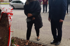 Wójt Gminy Roman Adamczyk wraz z kobietą składa kwiaty przy tablicy pamięci. W tle widać grupę uczestników wydarzenia. Wójt Gminy Roman Adamczyk wraz z kobietą składa kwiaty przy tablicy pamięci. W tle widać grupę uczestników wydarzenia.