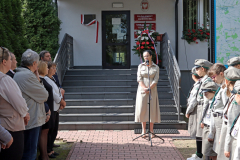 Prof. Sabina Bober stoi przy mikrofonie przed schodami prowadzącymi do budynku. Po obu jej stronach stoją uczestnicy wydarzenia, również harcerze