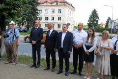 Około dziesięciu osób stoi na chodniku na zewnątrz w porze letniej, Są to uczestnicy uroczystości odsłonięcia tablicy