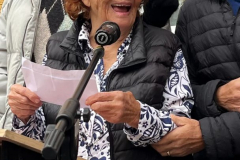Żydowskiego pochodzenia mieszkanka USA odczytuje z kartki przemowę stojąc na mównicy. Z dużym uśmiechem spogląda w stronę innych uczestników wydarzenia. Obok niej stoi dwóch mężczyzn - jeden starszy i jeden bardzo młody.