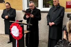Ksiądz proboszcz odczytujący przemowę na mównicy. Towarzyszą mu Ksiądz Biskup Mieczysław Cisło oraz Rabin Symcha Keller.