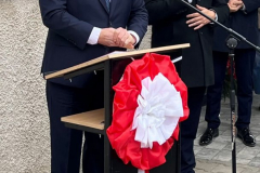 Marszałek Województwa Lubelskiego Jarosław Stawiarski stojący przy mównicy podczas odsłonięcia tablicy pamięci. Za nim mężczyzna przemawia do mikrofonu. Na zdjęciu widać również Burmistrza Andrzeja Kozinę.