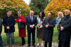 Uczestnicy wydarzenia stojący pod linią niskich drzew. Wśród nich, między innymi, konwersujący Marszałek Jarosław Stawiarki oraz Profesor Sabina Bober. Na zdjęciu obecni są również Rabin Symcha Keller oraz Biskup Mieczysław Cisło.