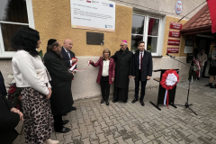 Marszałek Jarosław Stawiarski wraz z Leą Hirsch trzymają rozwiniętą biało-czerwoną kokardę zdjętą z tablicy. Otaczają ich inni uczestnicy wydarzenia, w tym, Profesor Sabina Bober, Ksiądz Biskup Mieczysław Cisło, Rabin Symcha Keller oraz Burmistrz Andrzej Kozina.