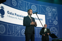 Wicemarszałek Michał Mulawa stoi przed mikrofonem i  udziela wypowiedzi. Za nim stoi konferansjer a w tle widać slajd wyświetlany na ekranie. Na slajdzie znajdują się widoczne części zegarka i napis w języku angielskim Gala passion for watches