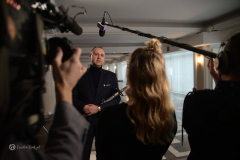 Aktor rozmawia z dziennikarzami podczas wywiadu, na zdjęciu znajduje się około czterech osób
