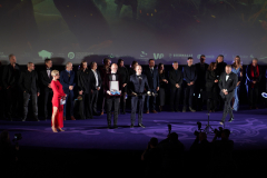 Konferansjerzy podczas premiery oraz aktorzy filmu, stoją wspólnie na scenie. Na pierwszym planie widać pierwsze rzędy publiczności