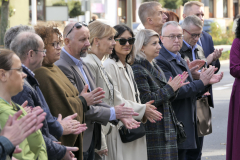 Około kilkunastu osób stoi na chodniku na ulicy. Wszyscy klaszczą w ręce