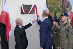 Wicemarszałek Piot Breś i Burmistrz Opola Lubelskiego Sławomir Plis, wspólne odsłaniąją tablicę pamięci  umieszczoną na fasadzie budynku. Obok nich widać dwóch żołnierzy WOT