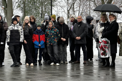 Młodzież szkolna i dorośli stoją na zewnątrz przed budynkiem podczas odsłonięcia tablicy pamięci