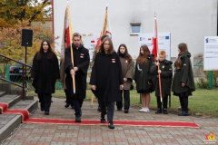 Młodzież z hufca harcerskiego w poczcie sztadarowym, około dziesięciorga dzieci stoi przed budynkiem, troje z nich trzyma chorągwie