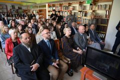 Wnętrze biblioteki miejskiej gdzie w jednej z sal siedzi na krzesłach kilkadziesiąt  osób w tym w pierwszym rzędzie rabin