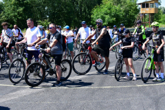 Kilkudziesięciu uczestników rajdu głównie mężczyźni stoją na otwartym placu ze swoimi rowerami.