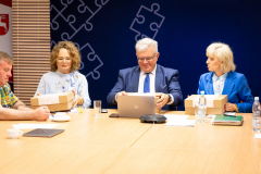 Dwie kobiety i dwóch mężczyzn którzy są uczestnikami spotkania siedzą wspólnie przy stole w sali konferencyjnej i rozmawiają