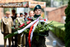 Żołnierka niesie wieniec biało-czerwonych kwiatów