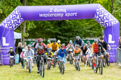 Rowerzyści przejeżdżający pod nadmuchaną bramą z napisem "Z dumą wspieramy sport".