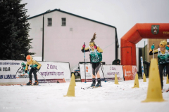 Dwóch zawodników ubranych stroje sportowe z nartami i kijkami przekracza linię startu podczas biegu