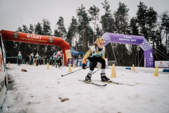 widok na zawodnika, dziecko, w pełnym zimowym stroju sportowym, ktory jedzie na nartach po trasie biegu