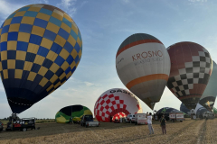 Na polu stoi kilka kolorowych balonów sportowych, część z nich jest już gotowa do startu, pozostałe dopiero napełniają się ciepłym powietrzem