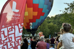 Kilkudziesięciu uczestników zawodów balonowych, spaceruje po chodniku, w tle widać wielki balon i baner z napisem lubelskie smakuj życie