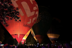 Cztery duże balony sportowe są ustawione na ziemi i oświetlone podczas nocnego pokazu