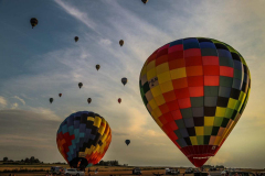 Na pierwszym planie widać dwa bardzo kolorowe balony sportowe stojące na ziemi i kilkanaście balonów szybujących w powietrzu