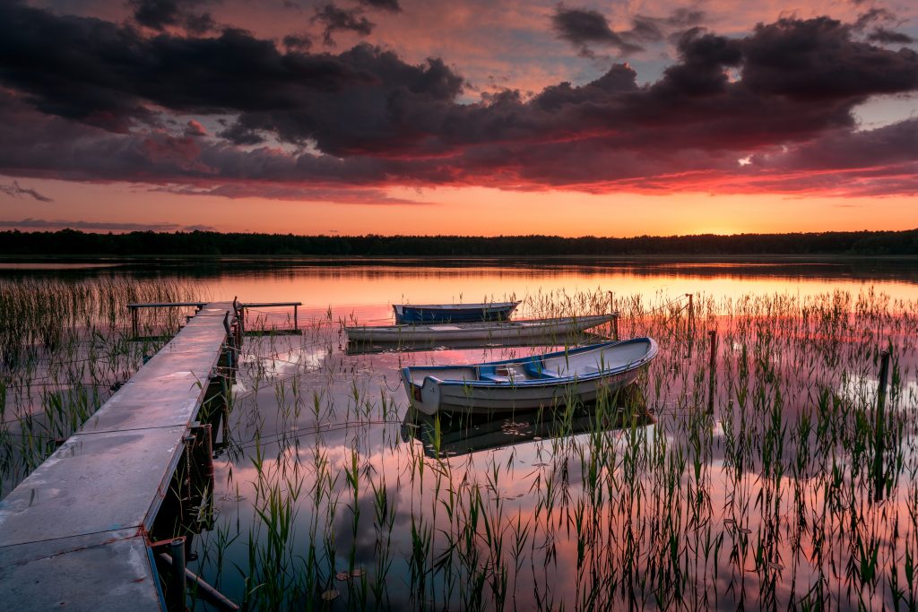 Jezioro, pomost, dwie łodzie, różowo -czerwone niebo, wspaniały zachód słońca.