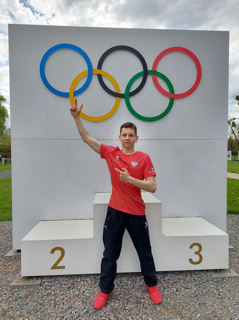 Na zdjęciu Rafał Wójcik w tle koła olimpijskie i podium